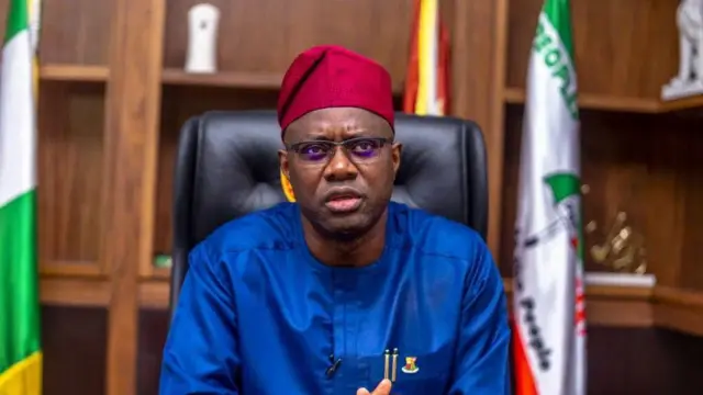 Gomina Seyi Makinde, o de fila pupa, wọ aṣọ alawọ aro, o si lo igo so oju rẹ, o n wo ọ̀ọ́kan.