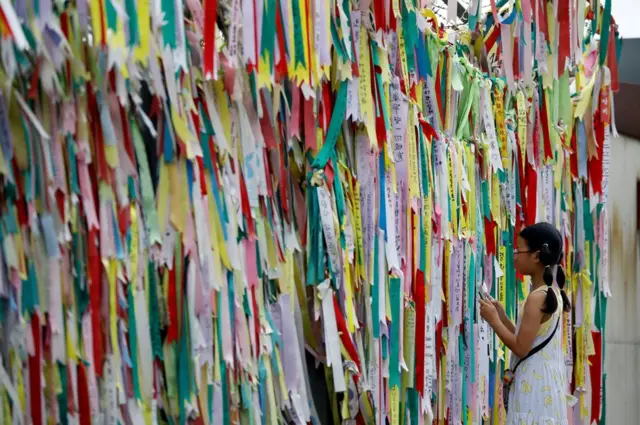 A girl looks at a fence covered with pastel ribbons