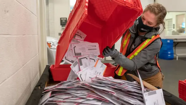 Una trabajadora postal con una cesta llena de votos por correo.