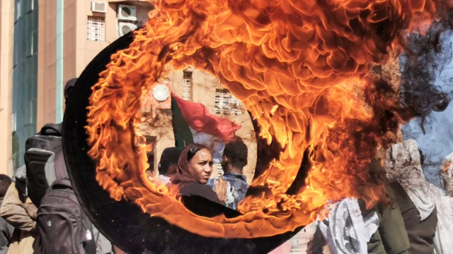 A ranar Talata, ɗaya daga cikin masu zanga-zanga a birnin Sudan na Omdurman ke kallo ta bayan wata taya da aka cinna wa wuta a yayin wata zanga-zanga ta neman mulkin farar hula