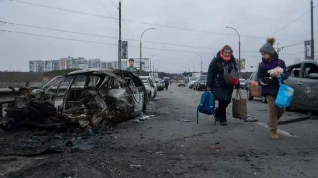 Mulher e criança segurando sacolas passandoqual site de aposta da bonus gratisfrente a carros incendiados