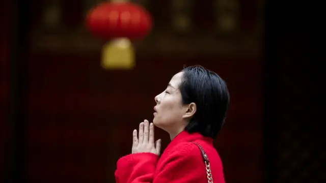 Mujer con manos juntas y lámpara detrás.