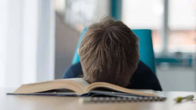 Niño con el rostro hundido en un libro en señal de frustración