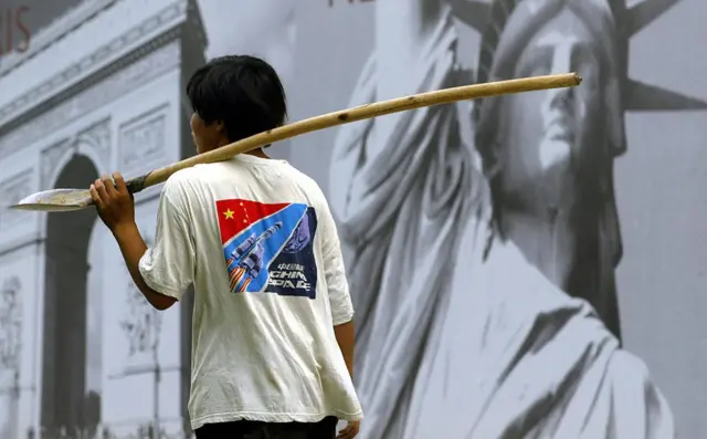 一名建築工作者走過北京一處豪華小區的廣告牌前,廣告牌背景是巴黎凱旋門與紐約的自由女神像。