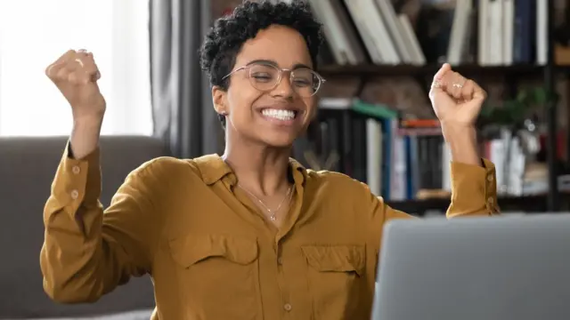 Mulher sentada, sorrindo e levantando os braçosbonus aposta sem depositocomemoração,bonus aposta sem depositofrente ao laptop