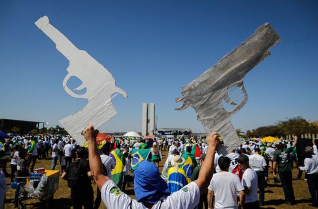 Um homem segura dois cartazes em forma de arma durante uma manifestação pró-armas em apoio ao presidente Jair Bolsonaro em Brasília, em 9 de julho de 2021