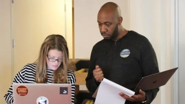 Una mujer y un hombre manejan un computador en una oficina.