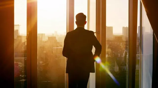 موظف ينظر من نافذة المكتب ويبدو أنه يتأمل في مستقبله الوظيفي