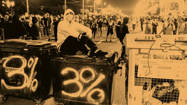 A protester sits atop a large rubbish container with a graffiti that reads '3%'.
