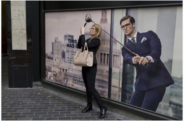 英国女性用手机在广告前留影