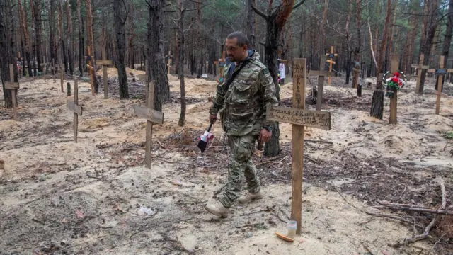 Soldado ucraniano caminha entre túmulossportingbet secivis e soldados ucranianos não identificadossportingbet seum cemitério improvisado na cidadesportingbet seIzium