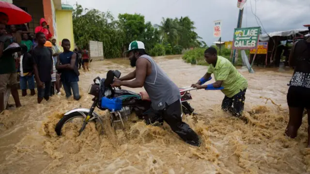 Hombres empujan una motocicleta en una zona inundada de Haití