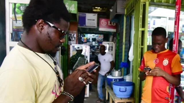 Two outside a shop looking at their mobile phones