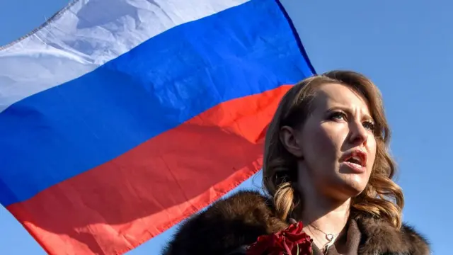 Ksenia Sobchak com a bandeira russa por trás