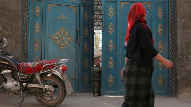 Woman walks past door with small child peeking out, Xinjiang (file pic)
