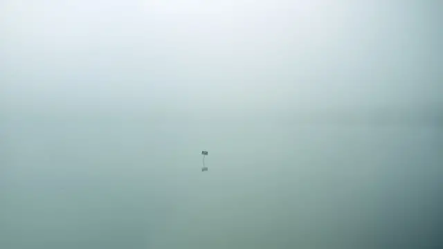 Un pequeño cartelito en la distancia en medio de un lago brumoso