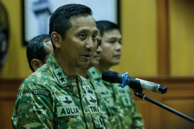 Kapuspen TNI Mayjen TNI Aulia Dwi Nasrullah menggunakan baju loreng sedang bicara di depan mikrofon.