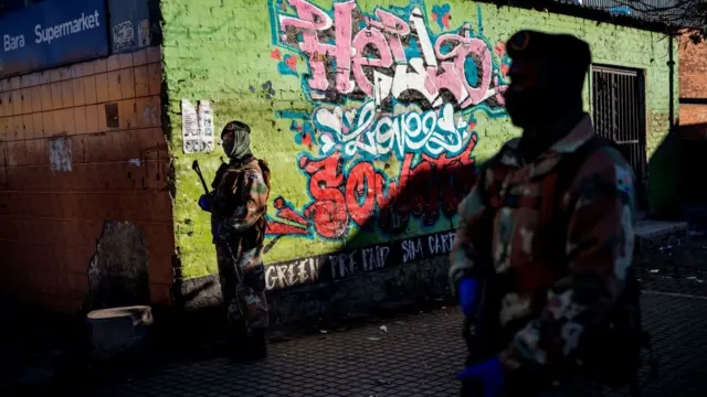 Des soldats de la South African National Defence Force (SANDF) patrouillent parmi les vendeurs de rue et les stands de nourriture à la station de taxis Bara à Soweto, Johannesburg, le 1er juin 2020,