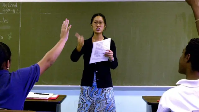 Students wey dey raise dia hand as teacher dey teach.