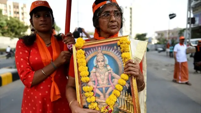 A woman holding a framed poster of a Hindu god followed by another woman