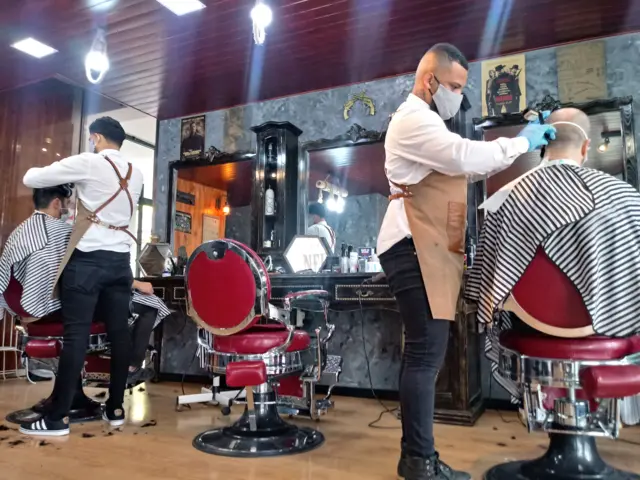 Barbeiros cortam cabelo de clientes