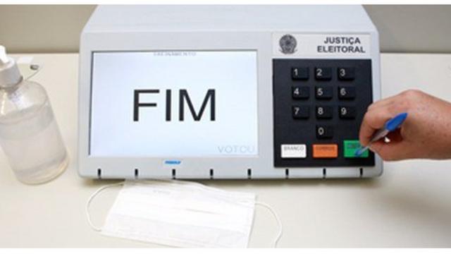 Uma mão pressiona o botão confirmadinheiro com apostas esportivasuma urna eletrônica com uma caneta