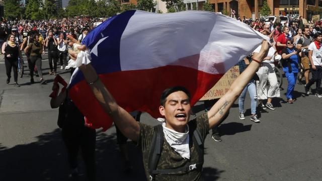Joven con una bandera de Chile delante de cientos de manifestantes.