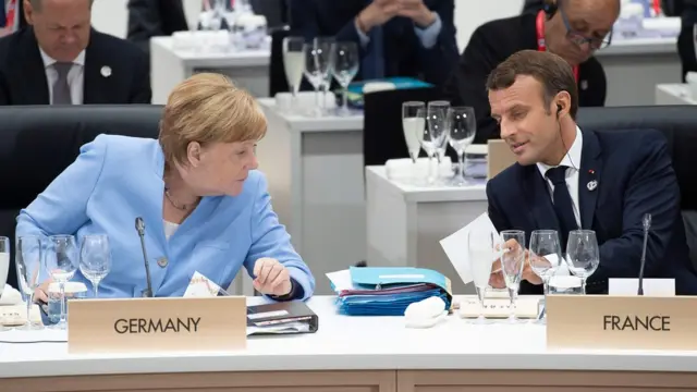 Angela Merkel e Emmanuel Macron se falam durante cúpula,7games baixar aplicativo esque aparecem sentados e com placas7games baixar aplicativo esseus respectivos países: Alemanha e França