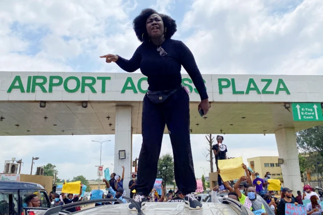 A demonstrator stands atop a vehicle and shouts slogans as others carry banners while blocking a road leading to the airport, during a protest over alleged police brutality, in Lagos, Nigeria - 12 October 2020