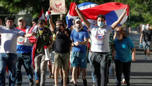 pessoas com máscaras e cartazes protestam na ruas