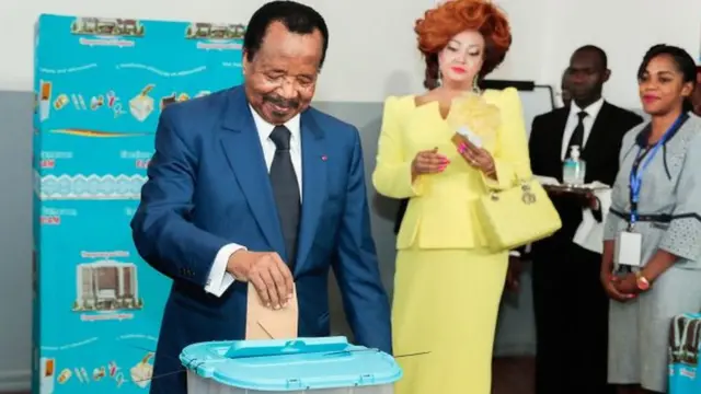 Le président du Cameroun et chef du Mouvement démocratique du peuple camerounais Paul Biya et son épouse Chantal Biya (en jaune) arrivent pour voter dans un bureau de vote lors des élections présidentielles à Yaoundé, Cameroun - 7 octobre 2018.