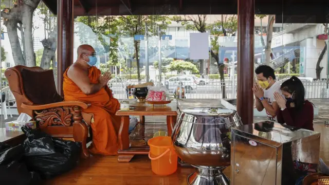 A Thai Buddhist monk wearing a protective mask receives devotees" offerings for Songkran celebrations in Bangkok,