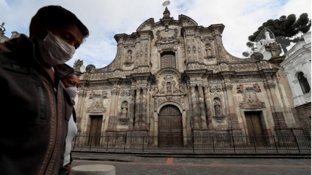 Des femmes masquées passent devant une église en Équateur