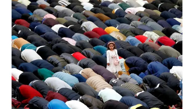 فتاة تقف وتنظر جانباً بينما يصلي المصلون أثناء الاحتفال بعيد الفطر في صالة دينامو الرياضية، في بوخارست، رومانيا.