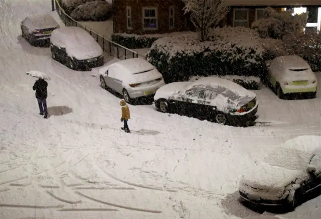 People walk along a snow covered road in Altrincham