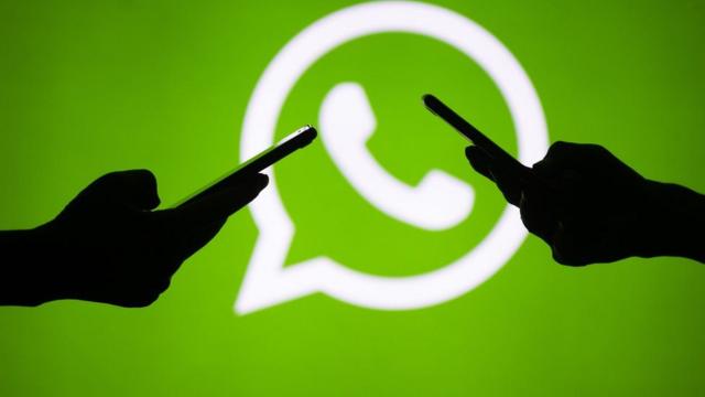 Sombra de dos personas manejando celulares con el logo de WhatsApp de fondo.