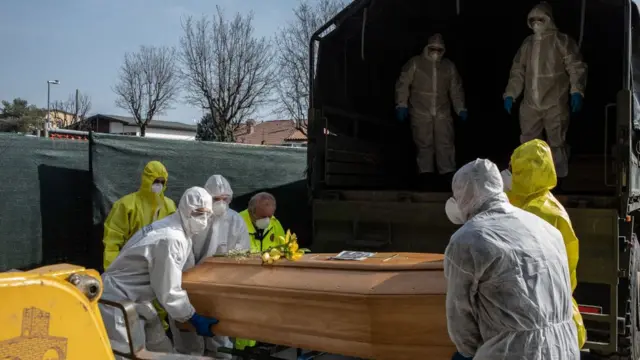 Люди в защитных костюмах держат гроб