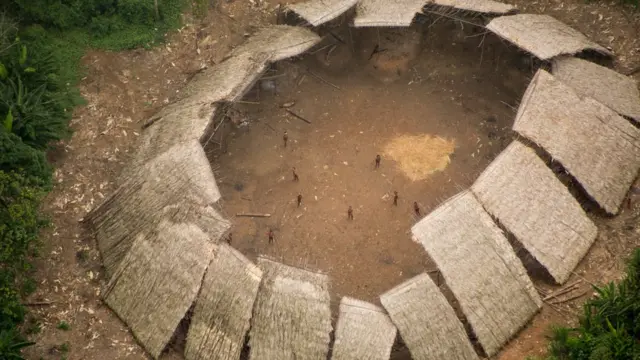 Maloca da comunidade Moxihatëtëma, formada por diversos telhados de palha voltados uns para os outros, com o centro aberto, em maio a clareira na floresta