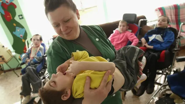 Una mujer sostiene a un niño con problemas motrices.