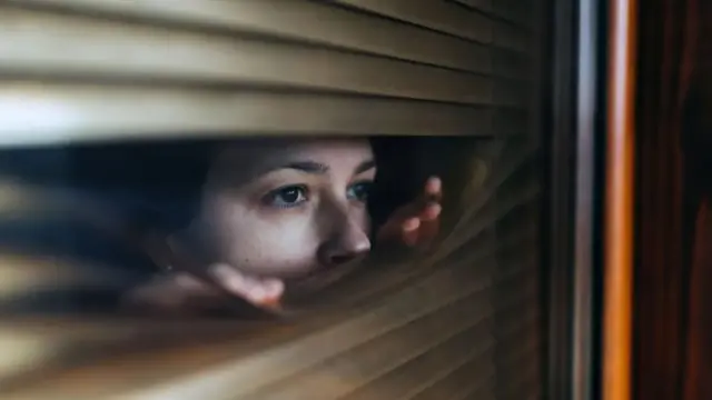 Una mujer mira entre persianas