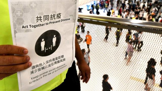 香港新界沙田新城市廣場購物中心內一名保安人員舉起維持社交距離提示海報（1/5/2020）