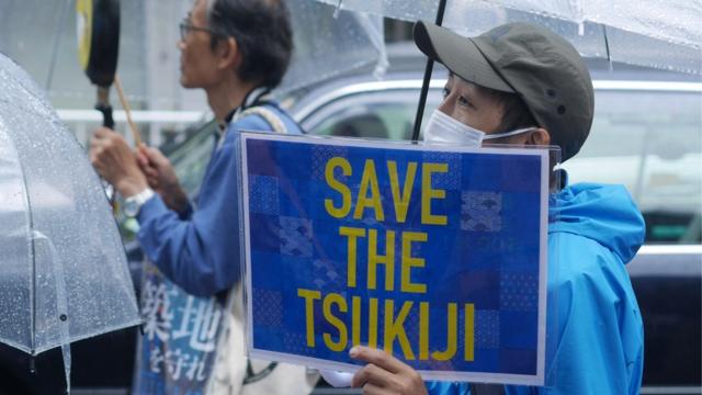 A protester stands in the rain with a sign saying Save the Tsukiji