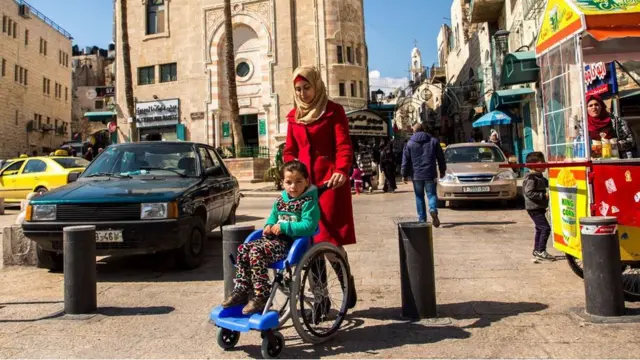 Madre llevando a niña en silla de ruedas en Palestina