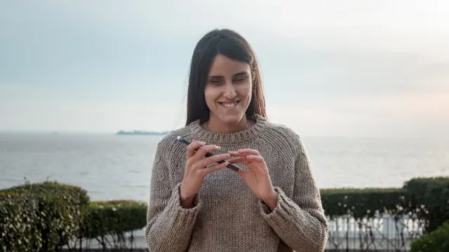 Milagros Costabel con su celular, por detrás se ve el Río Uruguay