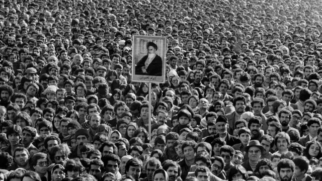 عکس آیت‌الله خمینی در دست افراد حاضر در افتتاحیه دانشگاه تهران. محمود احمدی نژاد، رییس جمهوری آینده ایران پایین سمت راست پشت مردی که کلاه خزدار به سر دارد