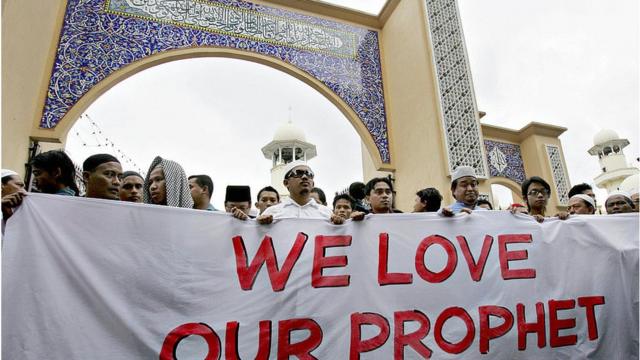 Manifestantes muçulmanos exibem uma faixa professando seu amor pelo profeta Maomé do lado de fora de uma mesquita antes de marchar em direção à embaixada dinamarquesa no centro de Kuala Lumpur