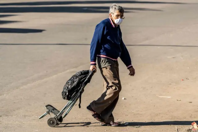 Un hombre mayor con un carro y mascarilla.