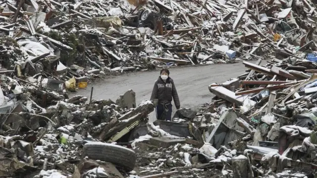 Uma mulher caminha entre os escombros na cidade japonesaesporte comMinamisanriku, no norte do Japão, após o tsunamiesporte com2011.