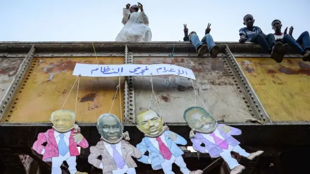 Des marionnettes en papier montrant l'ancien président Omar Al-Bashir et d'autres anciens responsables, avec le panneau en arabe "peine de mort pour les criminels du régime".