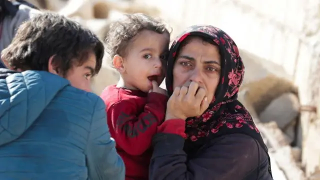 Une femme porte un enfant dasns les decombres